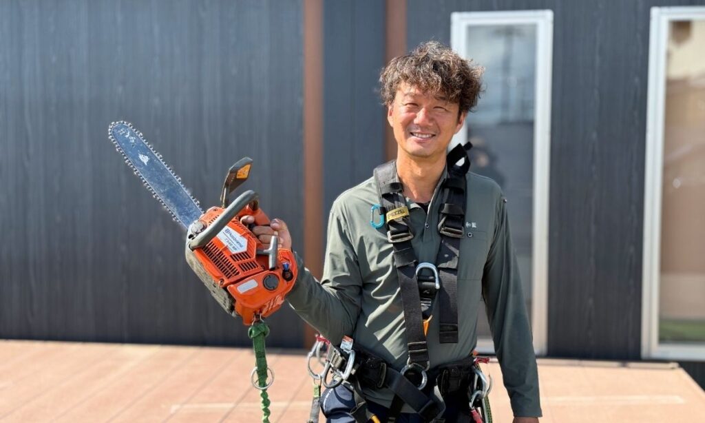 腰道具を着けてチェーンソーを持ってる笑顔のアーボリストの写真