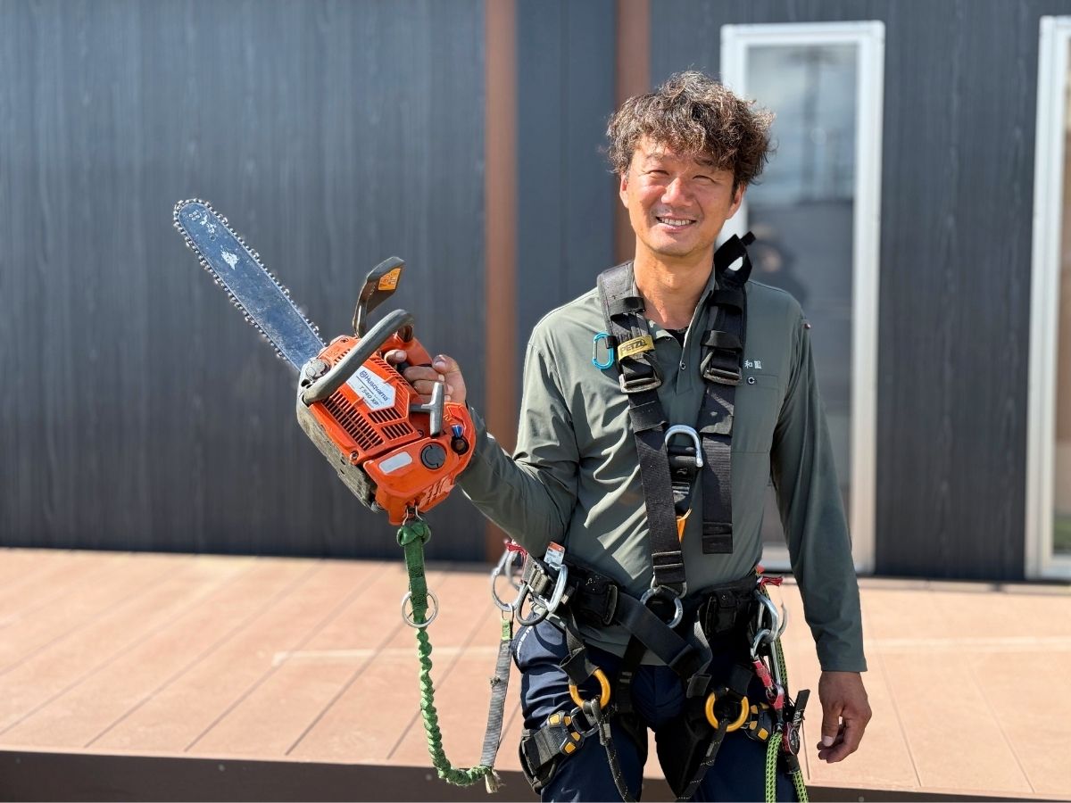 腰道具を着けてチェーンソーを持って笑顔のアーボリスト